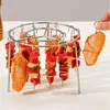 A hand is shown holding a chicken wing skewer, about to place it on a circular metal rack filled with various meat and vegetable skewers. Náhľad obrázku produktu