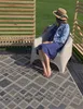 A woman sits in a chair on a patio next to a wooden screen, with a rug in front of her. Produktbild-Vorschau