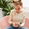 A young girl sitting in a pink chair, holding a colorful ball toy. Produktbild-Vorschau