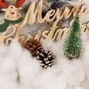 A close-up of Christmas decorations including a wooden 'Merry Christmas' sign, pine cones, and a miniature Christmas tree, all nestled in artificial snow. Náhled obrázku produktu