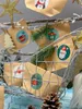 A close-up view of a DIY advent calendar set with small brown paper bags decorated with Christmas-themed stickers, hanging from a branch-like structure. Produktbild-Vorschau
