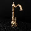 A vintage-style bronze faucet is displayed against a black background, resting on a bed of dark, rough material. Podgląd zdjęcia produktu