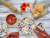 A flat lay of a colorful floral patterned dinnerware set, with a rolling pin, flowers, and baked goods. Náhľad obrázku produktu