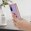 A hand holding a purple phone case with a gold trim and a ring holder. A vase with flowers is in the background. Anteprima dell’immagine prodotto
