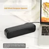 A black USB computer speaker is placed on a light-colored wooden surface next to a laptop. Produktbild-Vorschau