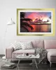 A framed picture of a sunset over the ocean with a palm tree in the foreground, displayed above a pink sofa in a living room. Produktbild-Vorschau