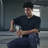 A man is kneeling and using a pipe cutter on a metal pipe in what appears to be a workshop or industrial setting. Produktbild-Vorschau