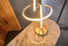 A modern table lamp with a gold base and a circular LED light is placed on a marble-topped table. Produktbild-Vorschau