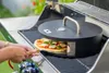 A pizza is being placed into a pizza oven attachment on a grill. Náhľad obrázku produktu