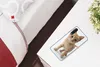 A phone case with a cat image on it is placed on a white table next to a bed. Produktbild-Vorschau