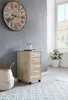 A roll container is placed next to a basket and a rug in a room with a large clock on the wall. Produktbild-Vorschau