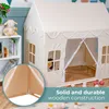 A cream-colored play tent shaped like a house, set up indoors with a bookshelf and toys nearby. A close-up inset shows the wooden frame construction. Produktbild-Vorschau
