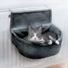 A cat is resting in a gray fabric hammock attached to a white radiator. Produktbild-Vorschau