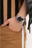 A person's wrist wearing a silver watch with a black face, with their hand in their pocket. Podgląd zdjęcia produktu