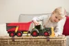 A young girl playing with a toy tractor and trailer on a woven basket. Produktbild-Vorschau