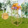A gold metal flower stand with a bouquet of orange and purple flowers on a grassy lawn with wedding decorations in the background. Náhled obrázku produktu