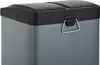 A close-up view of a grey dual-compartment trash can with a black lid and a silver handle. Produktbild-Vorschau