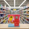 A product box for a handheld electronic game console is displayed on a wooden surface in front of blurred supermarket aisles. Náhled obrázku produktu