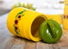 A yellow ceramic jar with sunflowers and a green lid lies on its side on a wooden surface. Produktbild-Vorschau