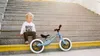 A young child sits on the steps next to a balance bike. Produktbild-Vorschau