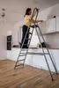 A woman is standing on a stepladder in a kitchen, cleaning cabinets. Podgląd zdjęcia produktu