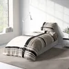 A bed with a duvet cover and pillow in a room with a window and a lamp. Produktbild-Vorschau