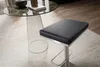 A modern bar stool is placed next to a glass-topped table with a metallic base, on a textured rug. Produktbild-Vorschau