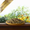 A wooden bowl filled with birdseed sits on a wooden surface, with a blurred background of greenery and yellow flowers. Produktbild-Vorschau