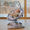 A baby is sitting in a baby bouncer in front of a large window with a winter landscape outside. Produktbild-Vorschau
