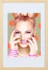 A woman with a bow-shaped hairstyle and vibrant makeup poses with her hands near her face, against a polka-dotted background. Produktbild-Vorschau