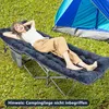 A woman is lying on a camping cot with a mattress pad next to a tent in a grassy area. Náhled obrázku produktu