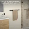 A bathroom scene showing a black towel rack mounted on a wall with a beige towel hanging on it. A sink and wooden cabinet are visible to the left, and a shower enclosure is on the right. Produktbild-Vorschau