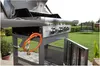 A gas grill with its lid open, set up in a backyard with a trampoline in the background. Podgląd zdjęcia produktu