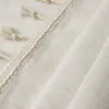 A close-up view of a cream-colored fabric with decorative tassels and trim. Produktbild-Vorschau