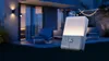 An outdoor motion sensor light is shown in a garden setting at dusk, with a patio and house in the background. Produktbild-Vorschau