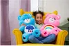 A young girl sits on a yellow armchair between two large plush Care Bears toys. Produktbild-Vorschau