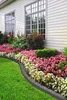 A beautifully landscaped garden bed borders a house, featuring a vibrant display of pink and white flowers, lush green grass, and a dark gray garden edging. Produktbild-Vorschau
