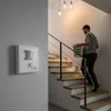A man walks up a staircase carrying a laundry basket, with a motion sensor mounted on the wall. Anteprima dell’immagine prodotto