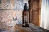 A bottle of cheese board oil sits on a wooden surface next to a textured stone wall. Produktbild-Vorschau