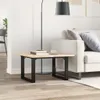A close-up shot of a wooden coffee table with black metal legs, placed next to a sofa in a living room. Podgląd zdjęcia produktu