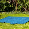 A blue picnic blanket with white dots is spread out on green grass in a garden setting, with trees and bushes in the background. Náhled obrázku produktu