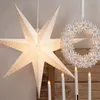 A large, white, star-shaped paper lantern with small perforations hangs next to a white snowflake wreath. Several white LED candles are arranged in a holder in the foreground. Podgląd zdjęcia produktu