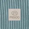 A close-up of a beige label with a bear logo and the brand name 'MISIOO' on a textured light blue background. Produktbild-Vorschau