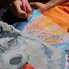 A person is working on a diamond painting kit, placing small beads onto a canvas. The painting appears to be of a dog's face with a colorful background. Produktbild-Vorschau