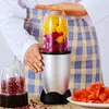 A person is using a portable blender to make a smoothie with fruits like dragon fruit and mango. Another cup with pomegranate seeds is visible. Produktbild-Vorschau