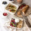 A lunchbox with compartments filled with food, including sandwiches, berries, yogurt, and granola, is arranged on a table with other food items and utensils. Podgląd zdjęcia produktu