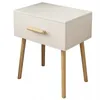 A white bedside table with a wooden drawer pull and wooden legs, shown against a white background. Náhľad obrázku produktu