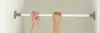 Two hands are shown adjusting a telescopic tension rod that is mounted between two walls. Produktbild-Vorschau