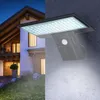 A solar-powered wall light is shown mounted on a wall next to a house at night. The light is illuminated, casting a bright glow. Produktbild-Vorschau