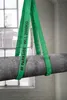 A heavy pipe is being lifted by green straps with text on them. Produktbild-Vorschau